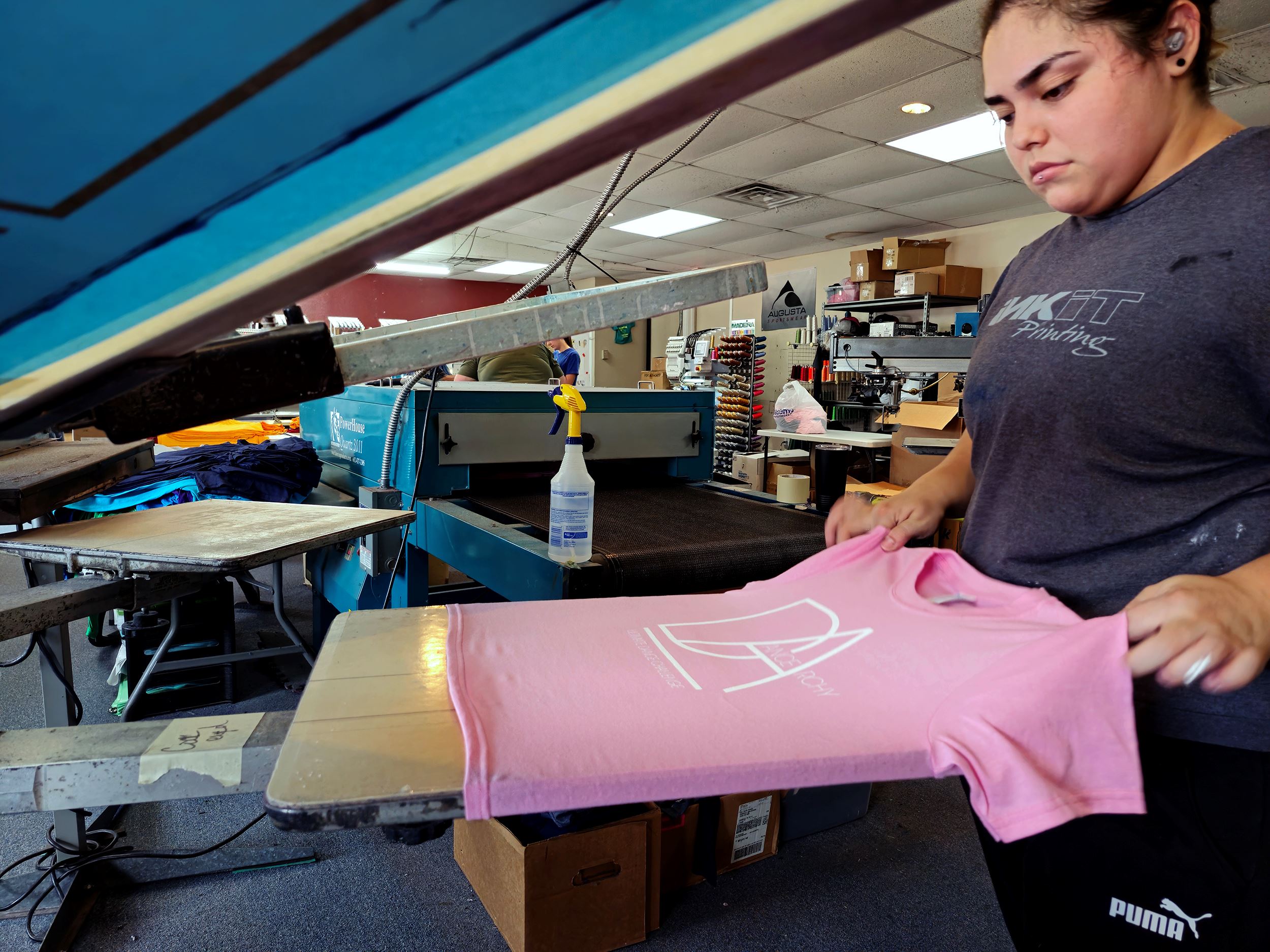 A screen printed t-shirt being pulled off the platen by employee