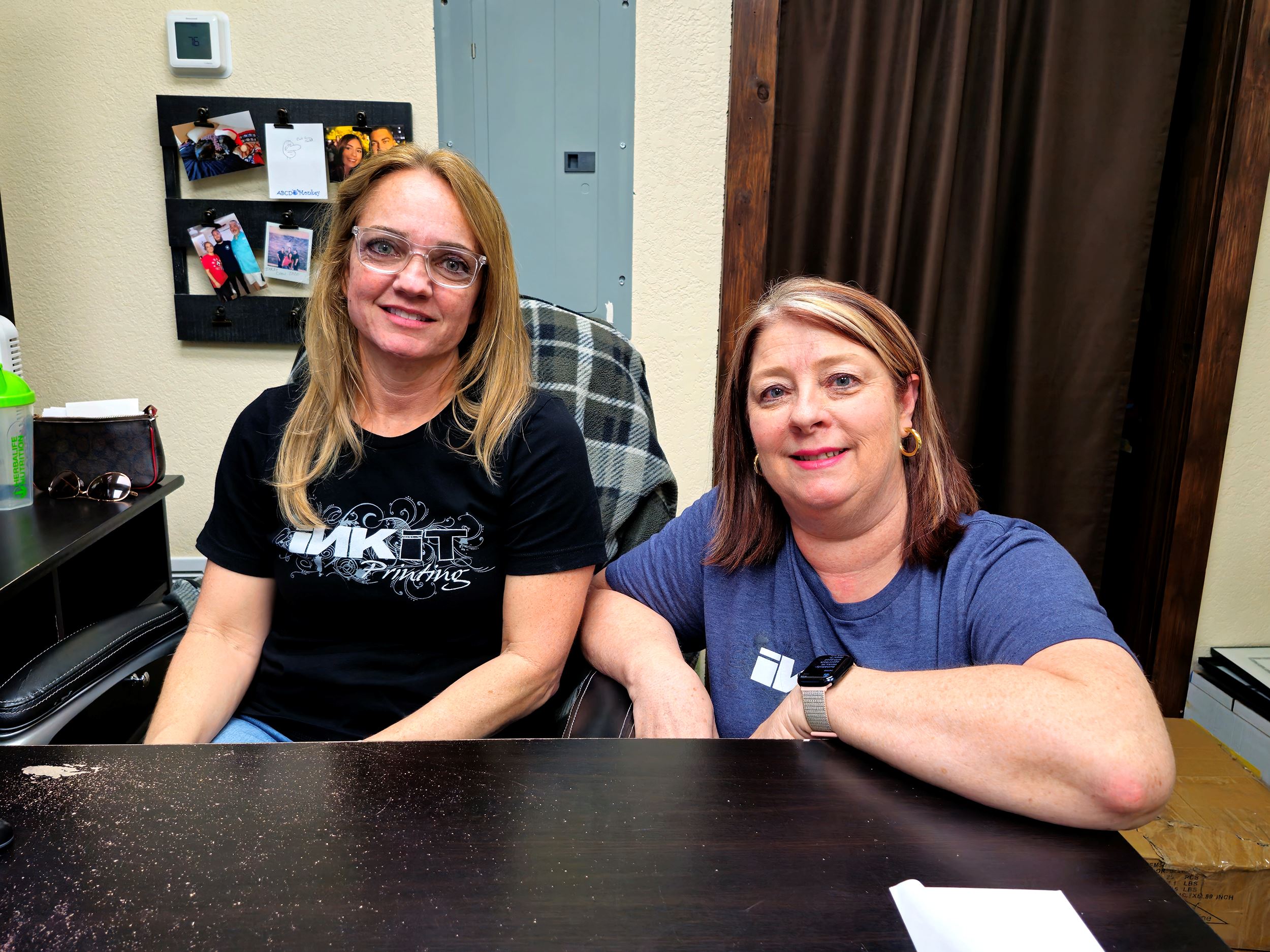 Shelly and Beth, Ink It Printing owners, stand together for a picture at their desk